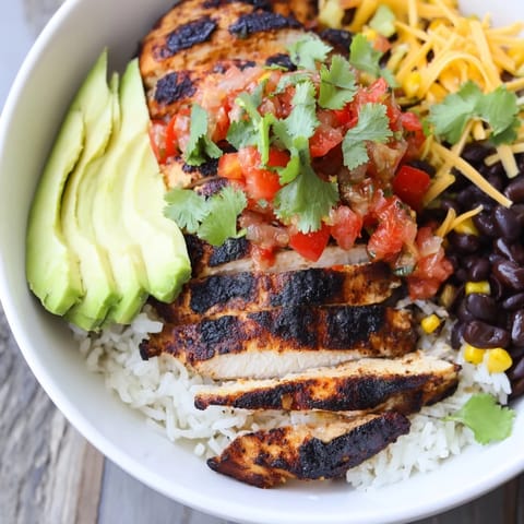A vibrant, gluten-free Spicy Chicken Burrito Bowl with charred grilled chicken, fluffy rice, black beans, sweet corn, fresh salsa, and creamy avocado slices.