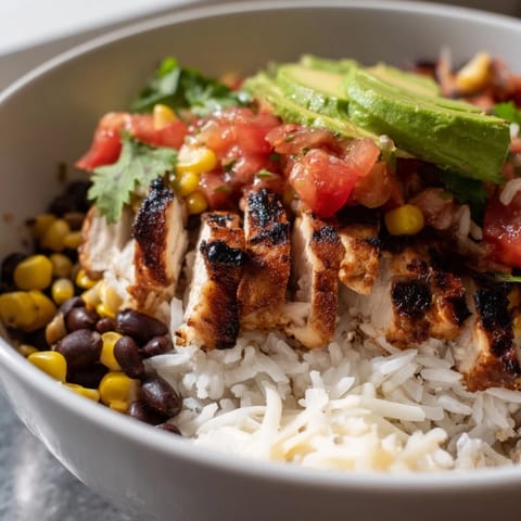 Hearty Spicy Chicken Burrito Bowl featuring juicy sliced chicken over rice, topped with warm black beans, sweet corn, zesty salsa, and melted Monterey Jack cheese.