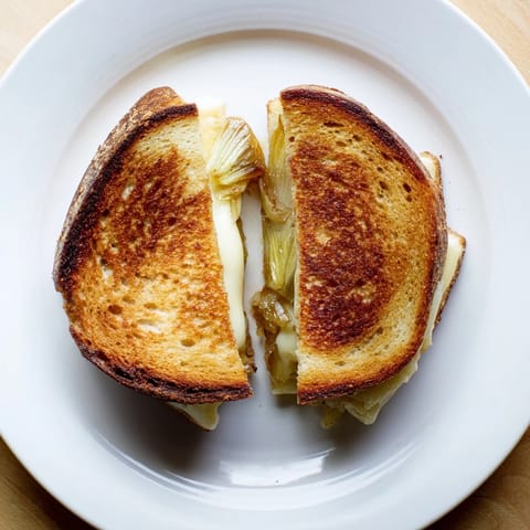 Golden slices of Havarti & Caramelized Leek Grilled Cheese melt between buttery, toasted sourdough, revealing sweet leek layers.