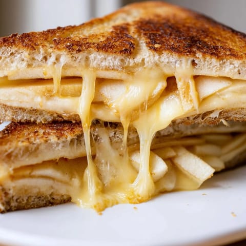 A close-up view shows buttery grilled bread with layers of smoky cheese and tart apple, perfect for a comforting lunch.  