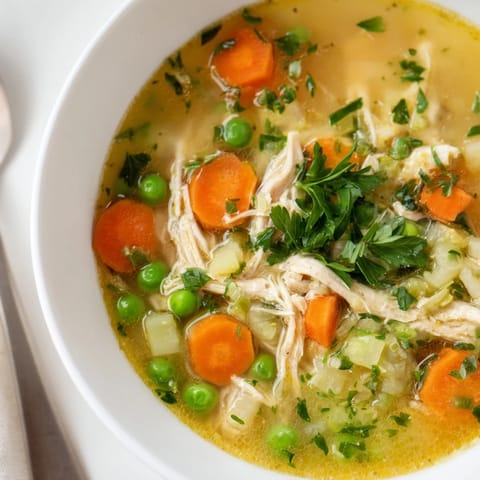 A warm bowl of Spring Garden Chicken Soup with tender shredded chicken, carrots, zucchini, and fresh parsley garnish.