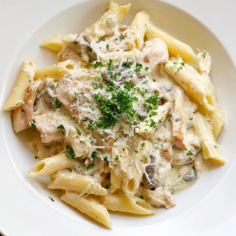 Serving Roasted Garlic Chicken Penne from a skillet with steam rising and crusty bread on the side