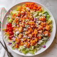 Freshly chopped romaine lettuce topped with spicy buffalo chicken, diced celery, and crumbled blue cheese in a white serving bowl.