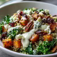 Fluffy quinoa topped with roasted sweet potatoes, massaged kale, cranberries, pecans, and blue cheese in a Harvest Kale Quinoa Bowl drizzled with lemon tahini dressing.