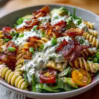 Creamy BLT pasta salad with crispy bacon, avocado, and cherry tomatoes in a tangy dressing, perfect for summer cookouts.